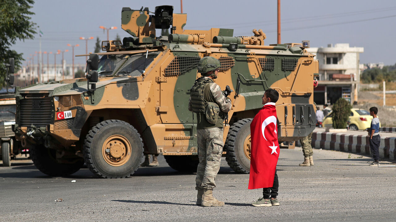 A boy wearing a Turkish flag stands next to a Turkish soldier in the town of Tal Abyad, Syria October 23, 2019.